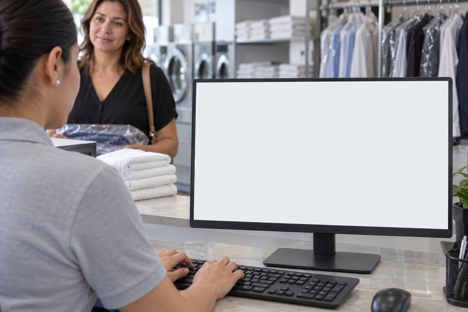 Recepcionista trabajando frente al monitor en una lavandería. Pantalla: Órdenes de servicio.